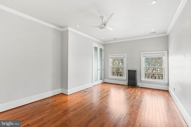 empty room featuring baseboards, ornamental molding, wood finished floors, and radiator