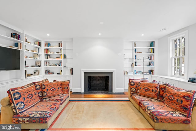 living room with a fireplace with flush hearth, built in shelves, wood finished floors, and recessed lighting