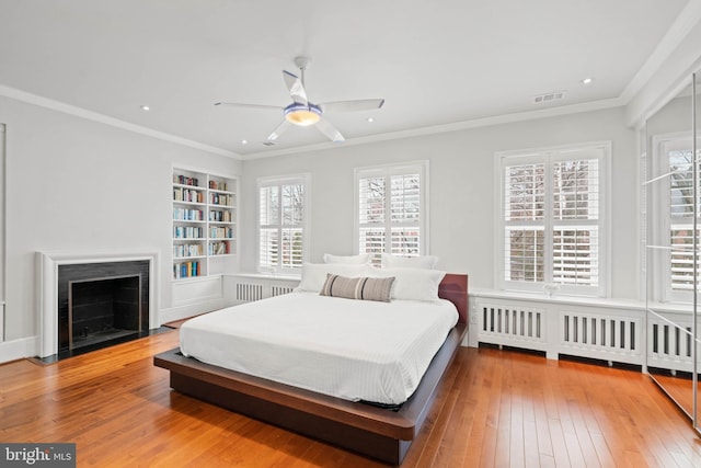 bedroom featuring a fireplace with flush hearth, visible vents, ornamental molding, radiator heating unit, and wood-type flooring