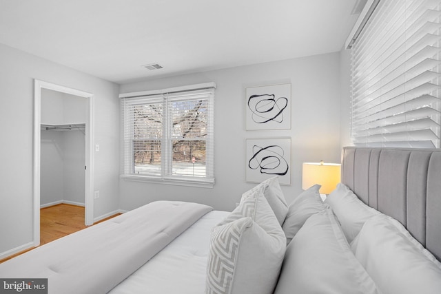 bedroom featuring visible vents, a walk in closet, baseboards, and wood finished floors