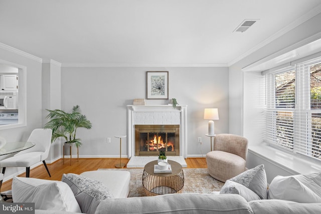 living area featuring visible vents, wood finished floors, a fireplace, and ornamental molding