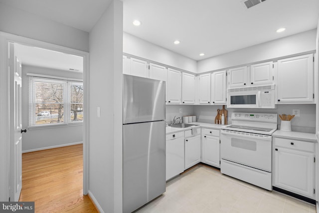 kitchen featuring white appliances, white cabinetry, light countertops, and baseboards