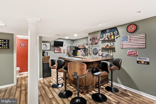 bar with decorative columns, a dry bar, baseboards, and wood finished floors