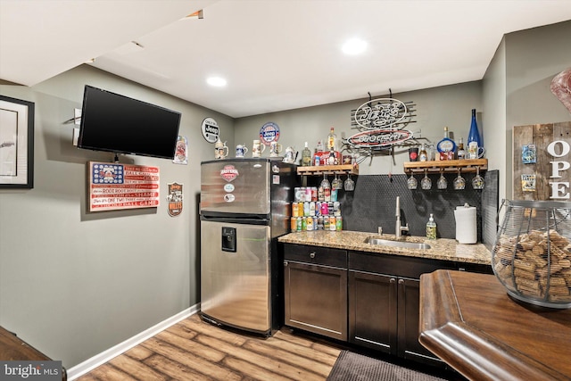 kitchen featuring light wood-style flooring, a sink, baseboards, freestanding refrigerator, and light stone countertops