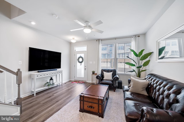 living area with ceiling fan, baseboards, wood finished floors, and stairs