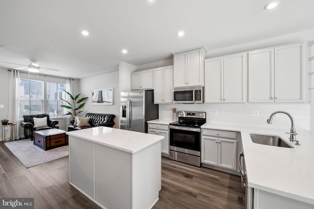 kitchen with a sink, a kitchen island, dark wood-style floors, appliances with stainless steel finishes, and ceiling fan