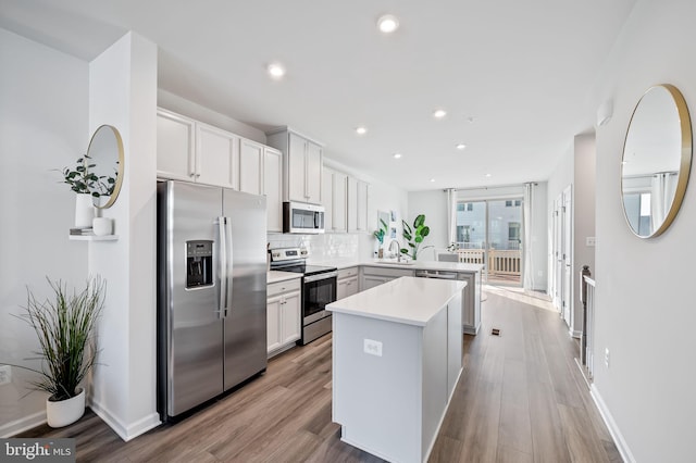 kitchen featuring light wood-style flooring, a peninsula, stainless steel appliances, and a sink