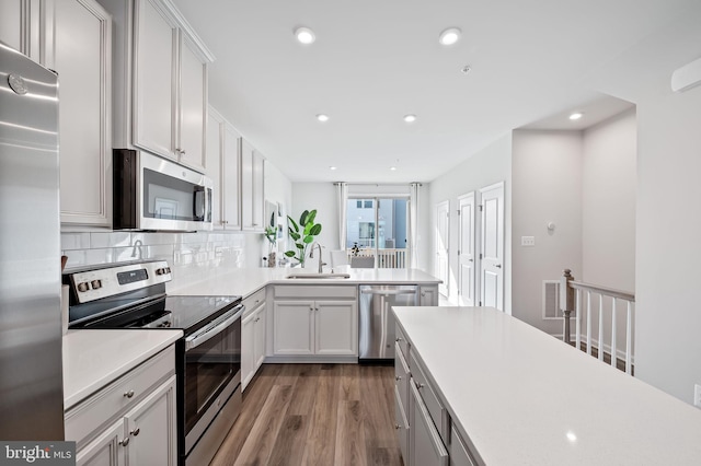 kitchen featuring a sink, backsplash, wood finished floors, appliances with stainless steel finishes, and light countertops