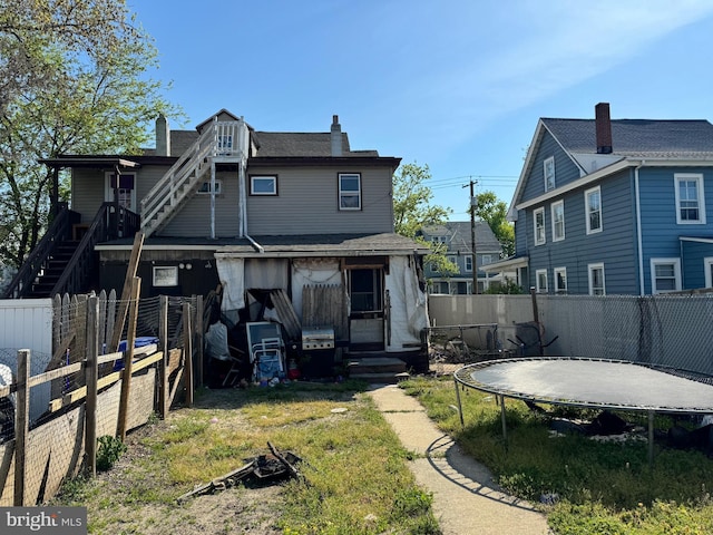 rear view of house featuring a trampoline, a chimney, and a fenced backyard