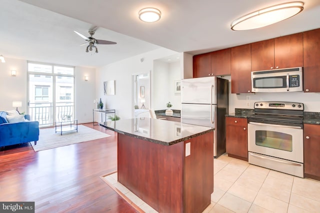 kitchen featuring dark stone counters, open floor plan, a center island, stainless steel appliances, and light wood-type flooring