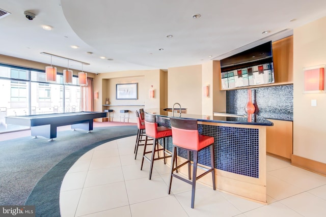 bar with a community bar, hanging light fixtures, backsplash, and light tile patterned floors