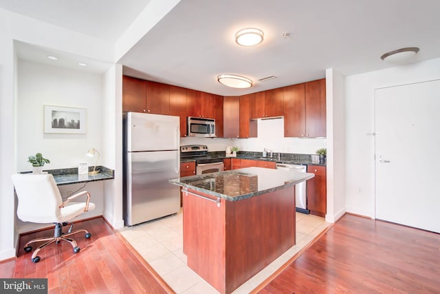 kitchen featuring stainless steel appliances, dark stone counters, a sink, and light wood-style flooring