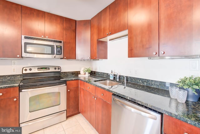 kitchen with dark stone counters, appliances with stainless steel finishes, light tile patterned floors, and a sink