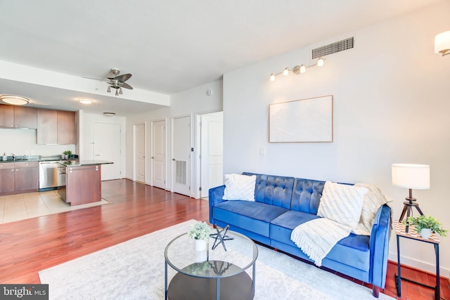 living room with light wood-style floors, baseboards, visible vents, and a ceiling fan