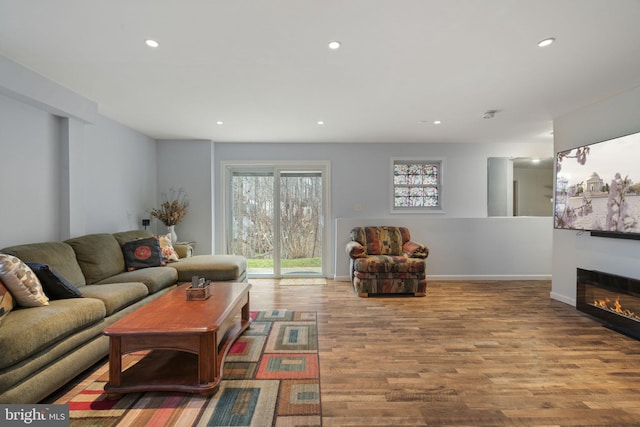 living area featuring a glass covered fireplace, recessed lighting, baseboards, and wood finished floors