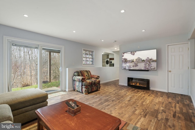 living room with a glass covered fireplace, wood finished floors, recessed lighting, baseboards, and washer / dryer