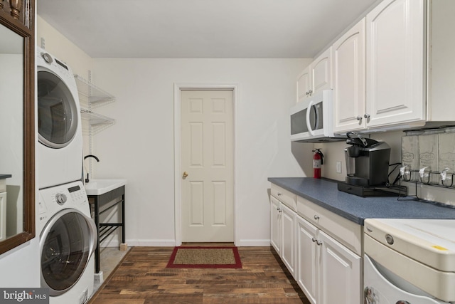 washroom featuring dark wood-style floors, baseboards, laundry area, a sink, and stacked washer and clothes dryer