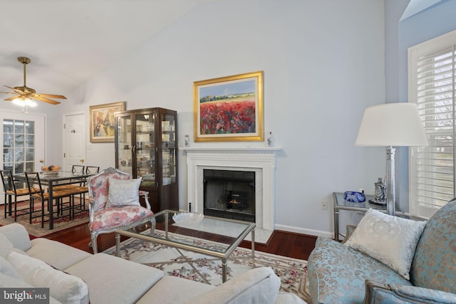 living area featuring a fireplace with flush hearth, wood finished floors, baseboards, ceiling fan, and vaulted ceiling