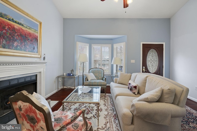 living area with dark wood finished floors, baseboards, a fireplace, and a ceiling fan