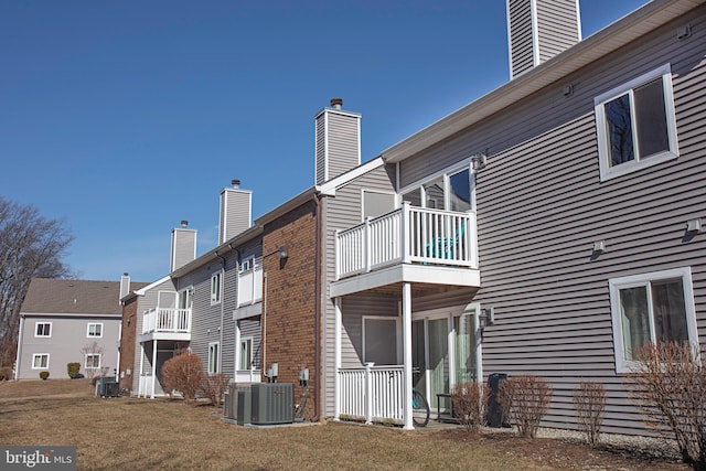 rear view of property with central AC unit, a balcony, a chimney, a yard, and brick siding