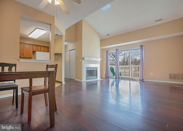 living room featuring baseboards, visible vents, dark wood finished floors, and a tiled fireplace