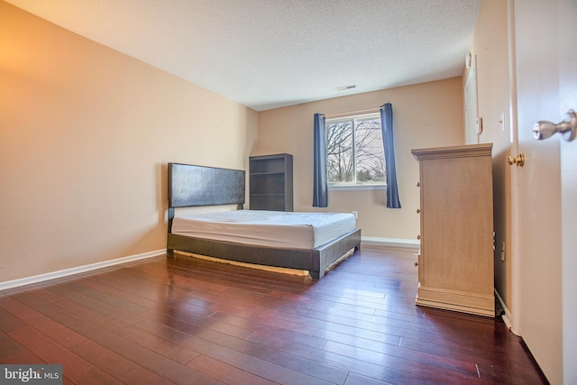 bedroom featuring a textured ceiling, hardwood / wood-style floors, visible vents, and baseboards