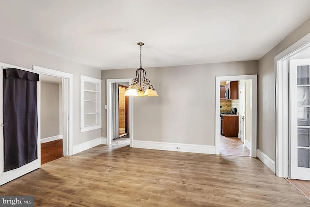 unfurnished dining area with a chandelier, light wood-style flooring, and baseboards