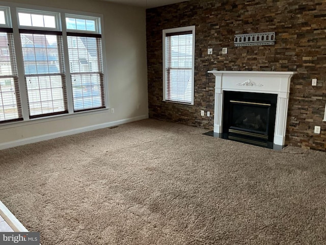 unfurnished living room featuring carpet, a fireplace with flush hearth, visible vents, and baseboards