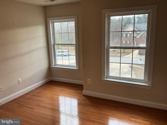 spare room with light wood-type flooring, plenty of natural light, visible vents, and baseboards