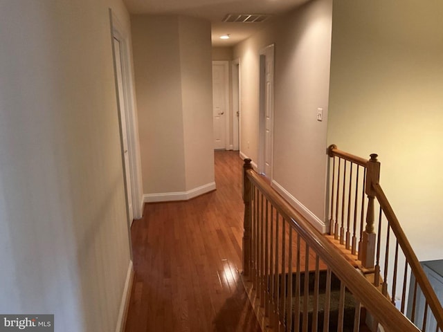 hall with baseboards, visible vents, an upstairs landing, and hardwood / wood-style flooring