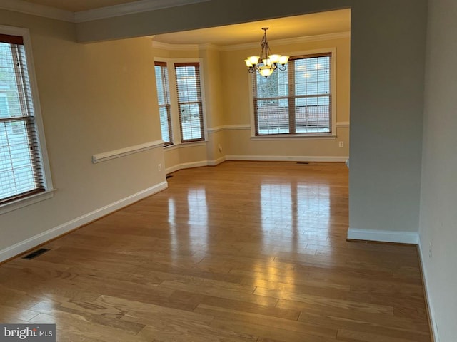 unfurnished room with a chandelier, a wealth of natural light, crown molding, and wood finished floors