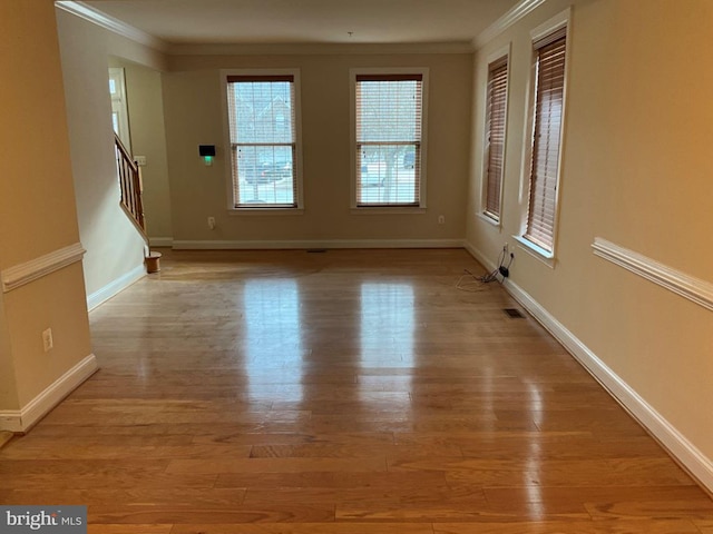 empty room with light wood finished floors, baseboards, stairway, and ornamental molding