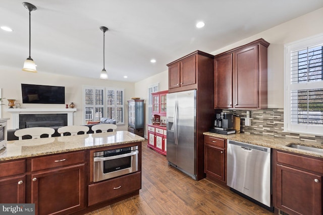 kitchen featuring decorative light fixtures, open floor plan, appliances with stainless steel finishes, a fireplace, and dark wood-style floors