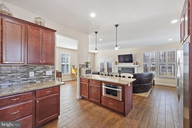 kitchen with dark wood finished floors, a fireplace, stainless steel appliances, open floor plan, and backsplash