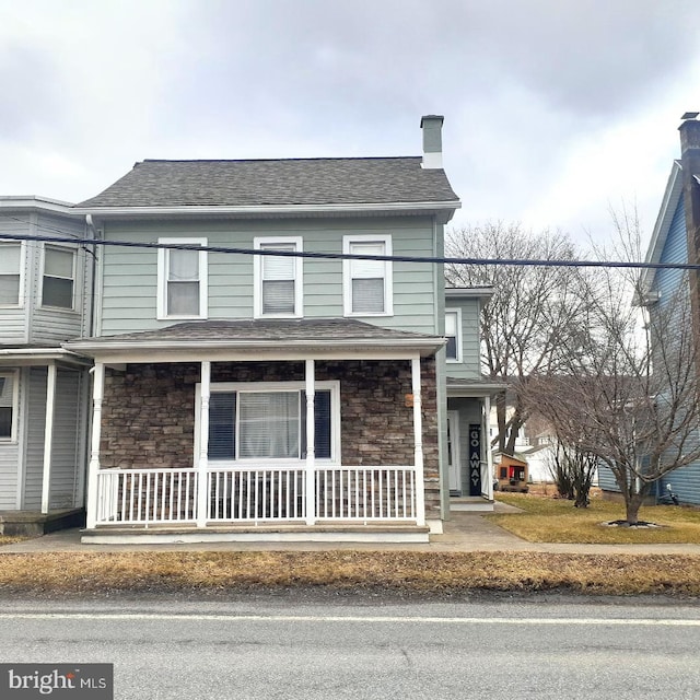 multi unit property featuring stone siding, covered porch, and roof with shingles