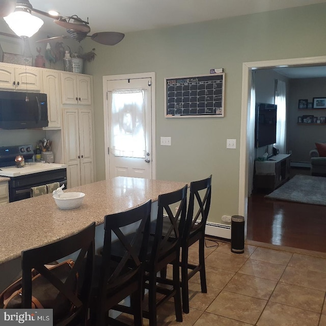 kitchen with light tile patterned floors, white cabinets, light stone countertops, black appliances, and a kitchen bar