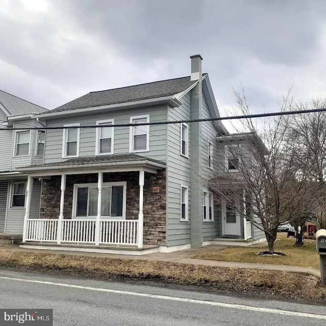 multi unit property with covered porch, stone siding, and a chimney