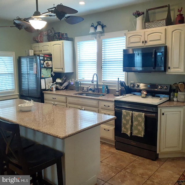 kitchen with light tile patterned floors, black range with electric stovetop, freestanding refrigerator, a sink, and light stone countertops