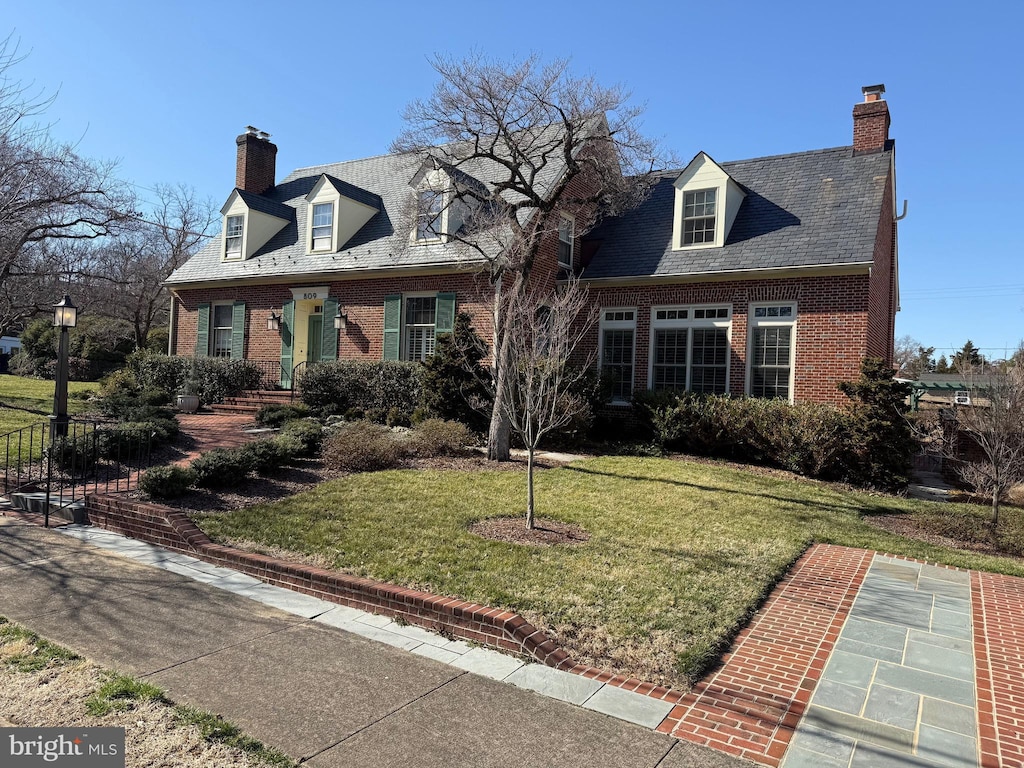 view of front of house with brick siding, a high end roof, a chimney, and a front yard