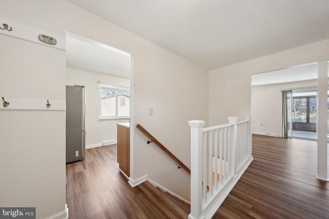 corridor with dark wood finished floors, baseboards, plenty of natural light, and an upstairs landing