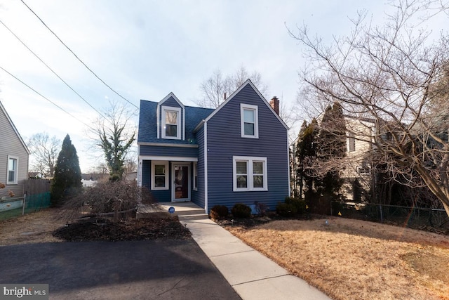 traditional home featuring roof with shingles, a chimney, and fence