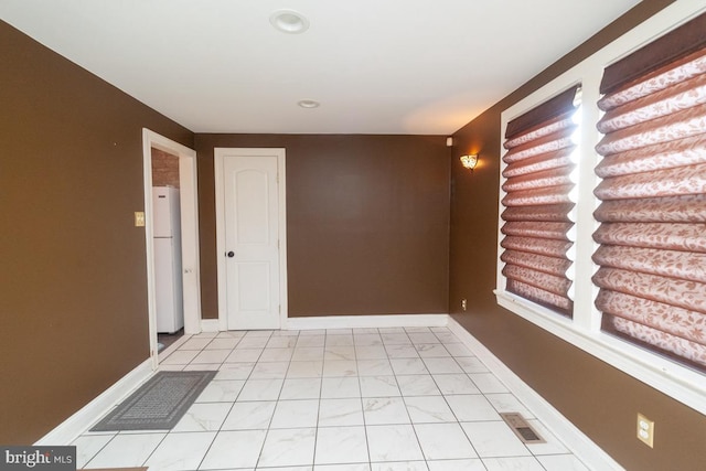 empty room with marble finish floor, baseboards, and visible vents