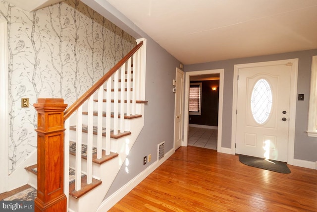 foyer entrance featuring wallpapered walls, visible vents, baseboards, and light wood finished floors