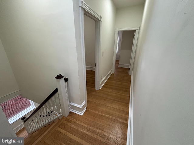 hall featuring light wood finished floors, baseboards, and an upstairs landing