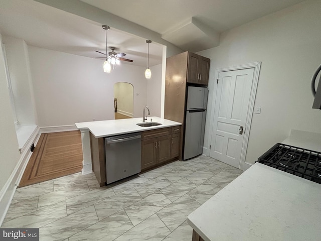 kitchen featuring arched walkways, appliances with stainless steel finishes, a peninsula, marble finish floor, and a sink