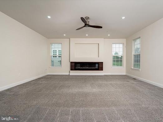 unfurnished living room with plenty of natural light, carpet flooring, a glass covered fireplace, and baseboards