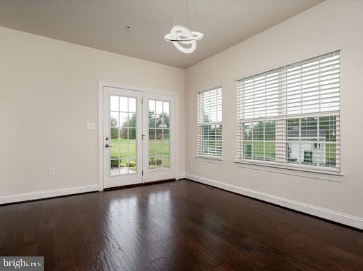 unfurnished room with an inviting chandelier, baseboards, and wood finished floors