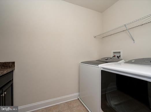 washroom with washing machine and dryer, cabinet space, baseboards, and light tile patterned flooring