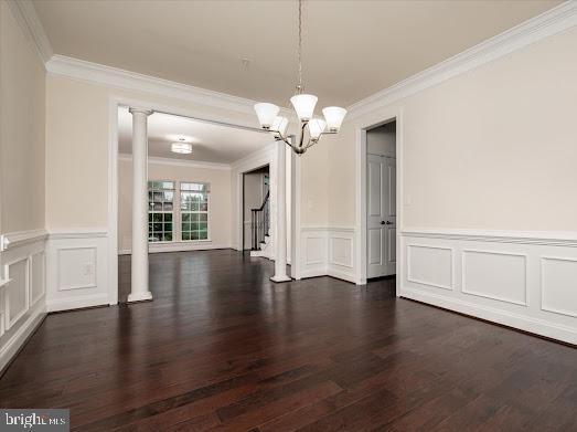 unfurnished dining area with decorative columns, stairway, an inviting chandelier, dark wood-type flooring, and ornamental molding