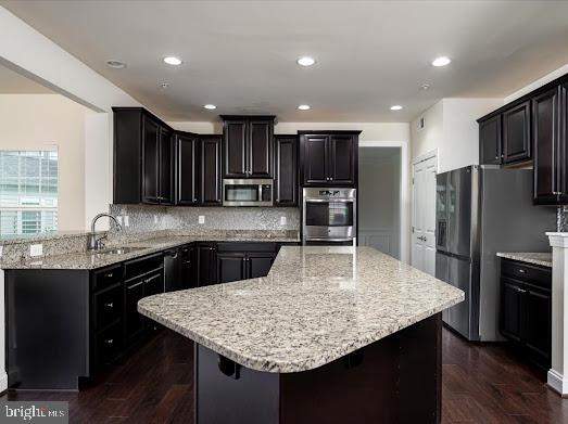 kitchen featuring a center island, stainless steel appliances, backsplash, a sink, and light stone countertops